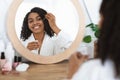 Skin nutrition. Beautiful black woman applying moisturizing serum on face at home