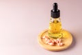 Skin rejuvenation concept - glass face serum bottle and songle use face oil capsules on a wooden plate on pink background. Copy