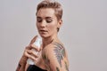 Skin with shine. Portrait of beautiful tattooed woman with short hair holding plastic bottle with skin care product