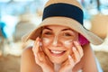 Skincare. Beauty Concept. Young pretty woman applying sun cream and touch own face. Female in hat smear sunscreen lotion on skin. Royalty Free Stock Photo