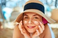 Skincare. Beauty Concept. Young pretty woman applying sun cream and touch own face. Female in hat smear sunscreen lotion on skin. Royalty Free Stock Photo