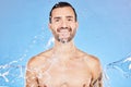 Skincare, portrait and water splash of man in studio isolated on a blue background. Health, cleaning and male model from