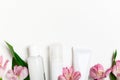 Skincare products bottles with lily flowers bottom border. Cream tube, concealer dispenser, micellar water blank plastic white Royalty Free Stock Photo