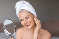 Skincare routine. Beautiful mature woman applying moisturizing cream, looking in mirror, enjoying new skin care products Royalty Free Stock Photo