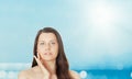 Skincare and sun protection in summer. Portrait of a beautiful young suntanned woman, blue sea and sky on background