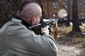 A skinhead male with the gun is threatening to someone behind the trees Royalty Free Stock Photo