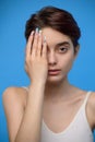 Skinny teenage girl cute girl hiding right half of her face with hand, at blue background