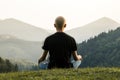 Skinny male person doing yoga sits in lotus position top of the hill in ukrainian carpathian mountains