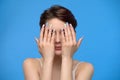 Skinny teenage girl cute girl hiding her face in her hands at blue background