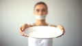 Skinny woman with taped mouth showing empty plate, concept of fasting, hunger Royalty Free Stock Photo