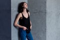 Skinny young European female model in casual clothes posing standing relaxed leaning on wall looking away from camera