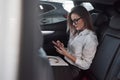 In the skirt. Smart businesswoman sits at backseat of the luxury car with black interior