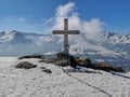 Skis, poles, and backpack by a big cross on the top of a mountain in winter