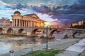 SKOPJE, MACEDONIA - APRIL 9, 2019: Old stone bridge over Vardar river and new building of the archaeological museum in the Royalty Free Stock Photo