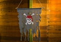 Skull and bones pirate banner hanging against wooden ship hull.