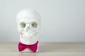 Skull sculpture in pink bow tie, bust, sculpture on the light background on the table. holiday background concept. Free space for