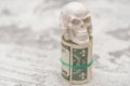 A skull standing on a bundle of money, twisted into a bundle