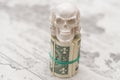 A skull standing on a bundle of money, twisted into a bundle