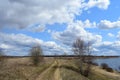 Sky, clouds. Winding road. River. Trees, shrubs, grasses on the low banks of the river. Forest in the distance. Rural view Royalty Free Stock Photo