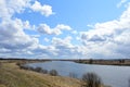 Sky, clouds. Winding road. River. Trees, shrubs, grasses on the low banks of the river. Forest in the distance. Rural view Royalty Free Stock Photo