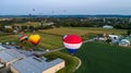 Sky filled with hot air balloons floating amongst a backdrop of suburban homes and buildings.