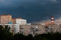 The sky is very dark blue over multi-storey buildings before a thunderstorm, with pipes visible on the horizon