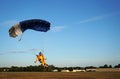 Skydiver under a small blue canopy of a parachute is landing on