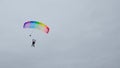 Skydivers with a multicolored parachute tandem in the air against a white sky