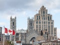 Skyline of Old Montreal, with Notre Dame Basilica in front, a vintage stone Skyscraper in background & a Canadian flag waiving. Royalty Free Stock Photo