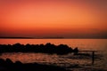 Skyline after sundown. Scenery of orange sky with rock silhouette and ocean waves. Orange sunset at shoreline photography.