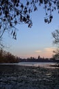 Skyline of a town seen from the distance over a lake at sunset framed by trees