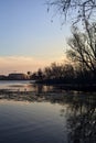 Skyline of a town seen from the distance over a lake at sunset framed by trees