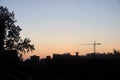 A skyline view of a lifting crane at down time with a background of sunrise and foreground of house roofs and tree branches Royalty Free Stock Photo