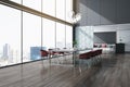 Skyline view from panoramic window in sunlit spacious high floor office hall with stylish grey meeting table and glossy red chairs
