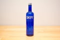 Skyy Vodka blue bottle on a wooden table with grey wall.