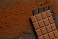 A slab of milk chocolate on top of a slab of dark chocolate on black slate dusted with cocoa powder from above. Space for text