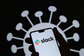 Slack logo on a smartphone silhouette hold in hand. Coronavirus image on the blurred background. Real photo, not a montage