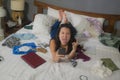 Slackness and chaos at home lockdown - young disorderly and chaotic Asian Korean woman on bed taking selfie with mobile phone on Royalty Free Stock Photo