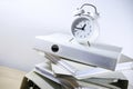 Slanted stack of ring binders and a white alarm clock on top reminding to the deadline, business concept of bureaucracy,