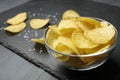 Slate board with bowl of potato chips on grey table, closeup Royalty Free Stock Photo