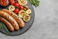 Slate plate with delicious barbecued sausages and vegetables on gray background. Royalty Free Stock Photo