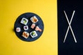 Slate plate with prawn sushi, avocado, raw fish, rice and salmon, with chopsticks on a half yellow half black background