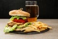 Slate plate with tasty burger, french fries and mug of beer on table Royalty Free Stock Photo