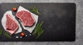 On a slate, a raw steak. On a background of dark shale are two raw steaks. Slice of pork seasoned with herbs, pepper, and salt.