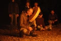 Slavonic shaman playing tambourine performing pagan ritual in front of a fire, people standing behind