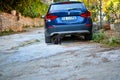 A sleek black cat sitting by a blue BMW sedan in an alley by a stone wall in the ancient village of Portovenere Italy
