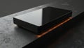 Sleek black rectangular object with glossy finish rests on dark textured surface, accented by subtle orange glow beneath. Royalty Free Stock Photo