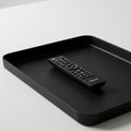 A sleek black remote control rests in a matching black tray on a white surface. The Royalty Free Stock Photo