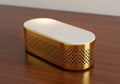 A sleek, gold-colored, perforated rectangular device resting on a wooden surface Royalty Free Stock Photo