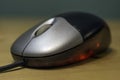 Sleek silver and black computer optical mouse with red light glowing against wooden desk table Royalty Free Stock Photo